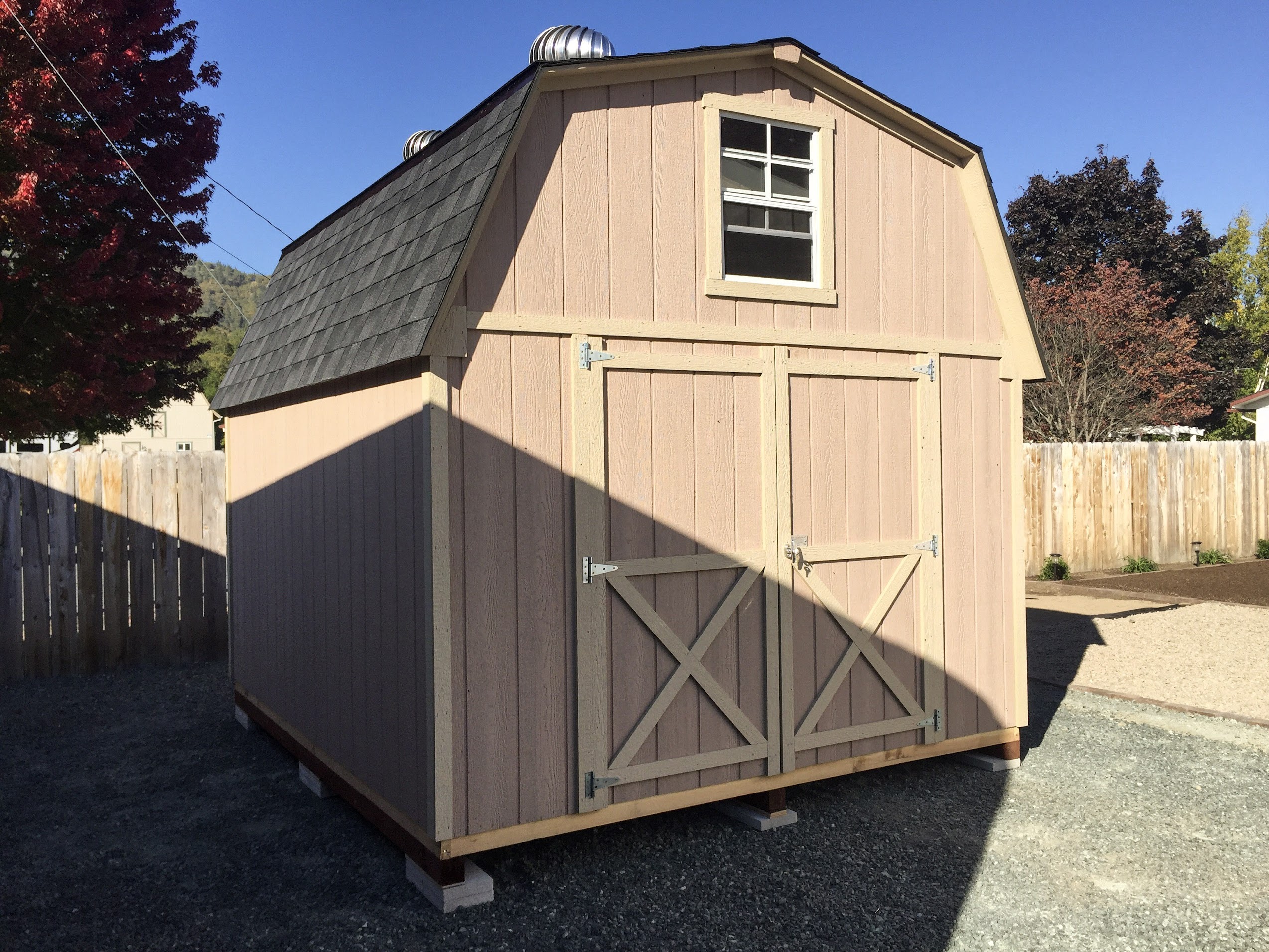Tan gambrel-roof barn-style storage building with double doors and upper window