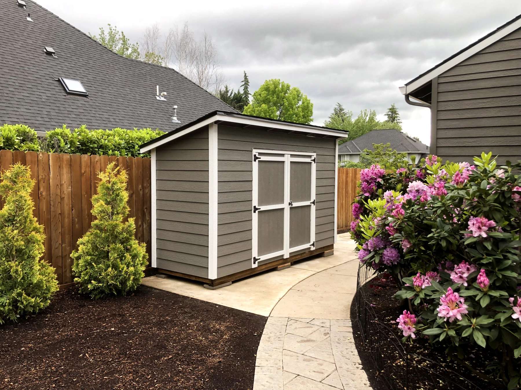 Gray lean-to shed with double doors beside a garden path.
