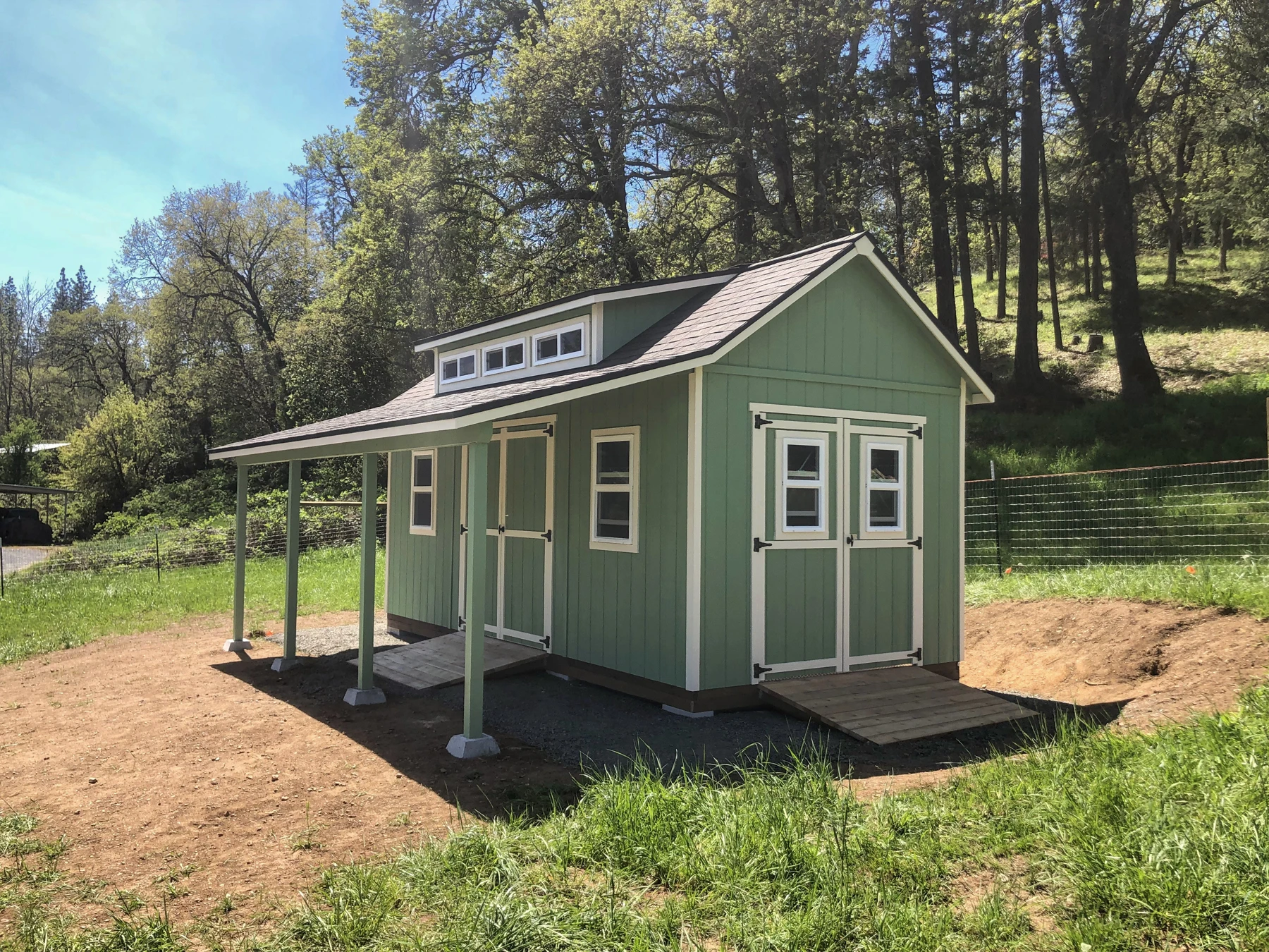Green shed with a covered porch, windows and a raised roof detail.